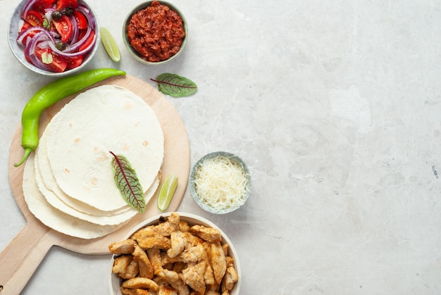 A table with a variety of ingredients including chicken, peppers, and onions.