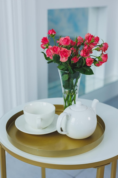 A table with a white teapot and a white cup on the table a vase with fresh flowers