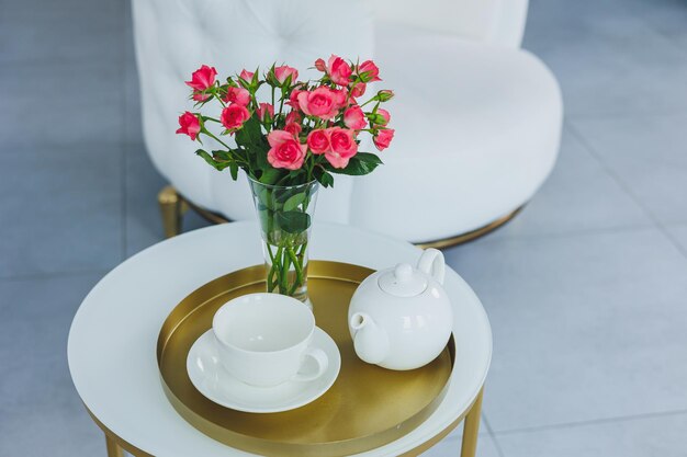 A table with a white teapot and a white cup on the table a vase with fresh flowers