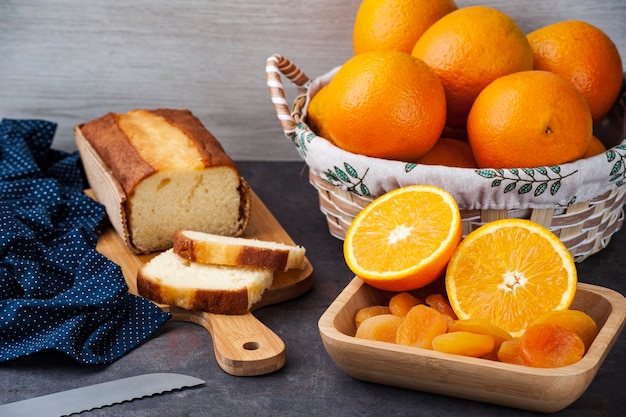 Table with whole and sliced oranges, dried apricot and orange cake on a kitchen board.