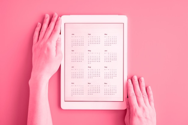 Tablet computer with app calendar for unspecified unknown date year without date in womans hands business or to do list goals top view flat lay toned in viva magenta trend color of the year 2023