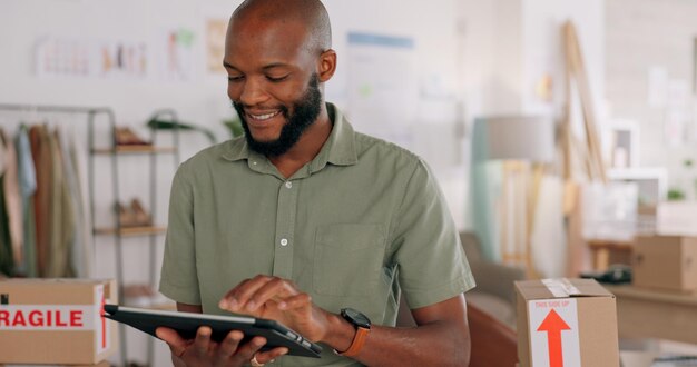 Tablet creative and online order with a black man designer working in a workshop for shipping or delivery Computer ecommerce and logistics with a male managing stock or the shipment of goods