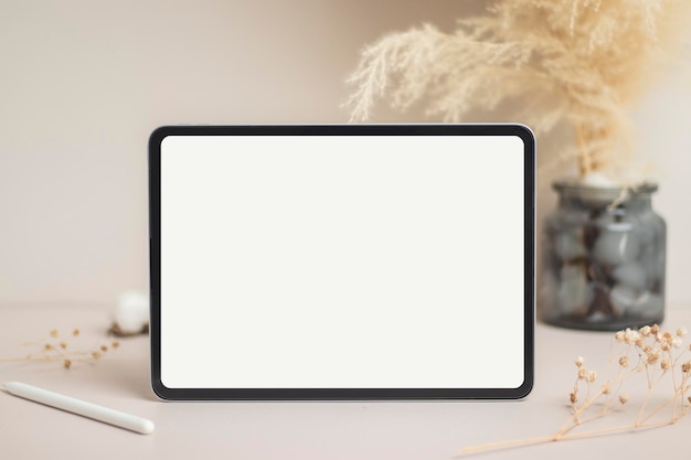 Tablet empty white screen with pencil mockup Cotton flower and dry leaves on beige background mockup for design