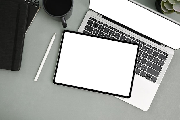 Tablet mockup on laptop keyboard stylus pen coffee cup and notepad on grey background