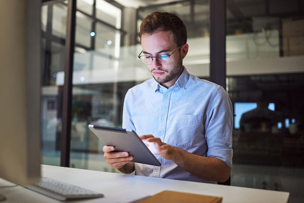 Tablet planning night research and businessman working on the internet in a dark office at work Business employee reading an email on the web with technology during overtime at a corporate company