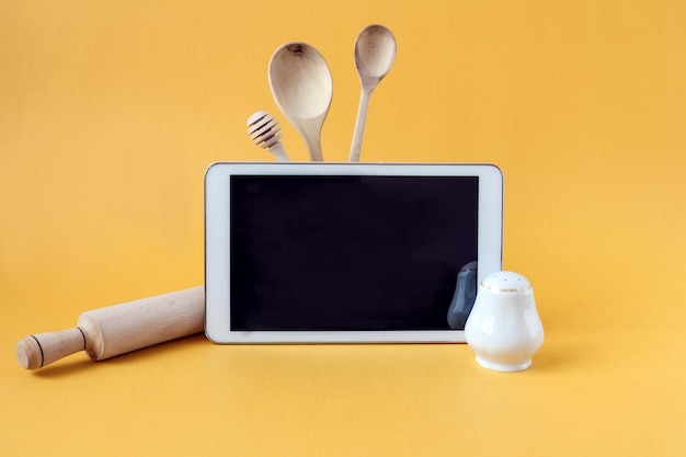 Tablet salt shaker kitchen utensils on a yellow background side viewthe concept of starting classes in cooking courses via the Internet