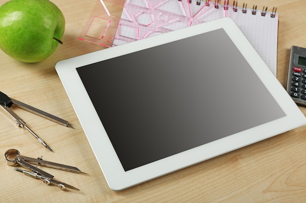 Tablet and school supplies on wooden table closeup