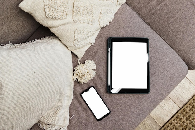 Tablet and smartphone with blank screen on sofa in living room Gadget mock up device layout