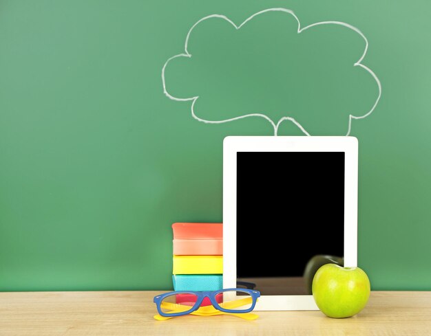 Tablet on table on green blackboard background