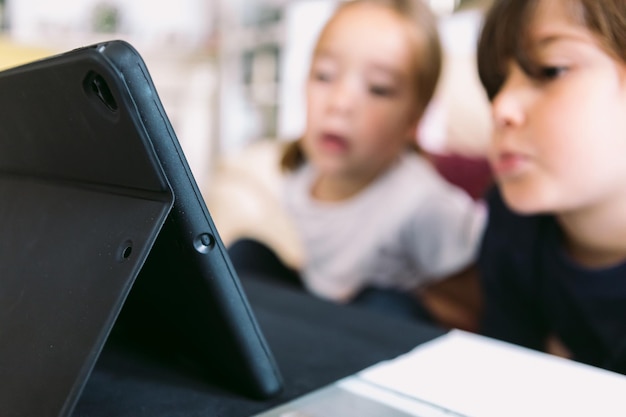 A tablet with a black cover and two girls in the background out of focus watching a video Concept of childhood technology learning having fun the Internet and connectivity