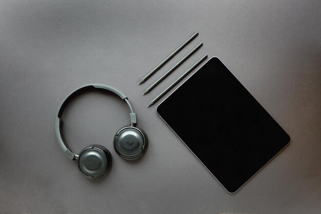 Tablet with pencils on black background designer working place using pen and headphones top view