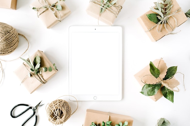 Tablet with tablet screen and beauty arrangement frame of craft boxes and green branches on white background.