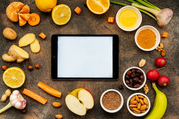 A tablet with a white screen around healthy foods to enhance immunity. Top view, copy space.