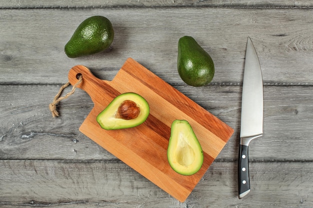 Tabletop view, avocado cut in half, seed visible, on a chopping board, chef knife, and two whole green pears next to in.