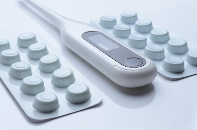 tablets in a package and a white electronic thermometer on a white surface close-up.