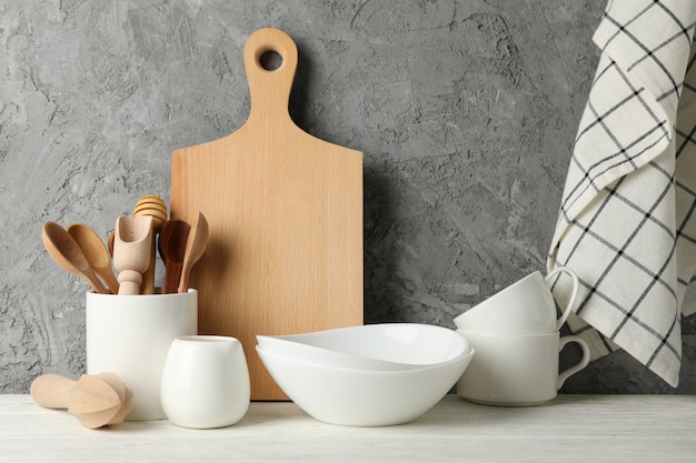 Tableware, cutlery and wooden board on white table against gray, space for text