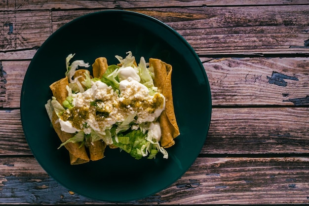 Tacos flauta with cheese cream and lettuce on a wooden table Mexican snacks