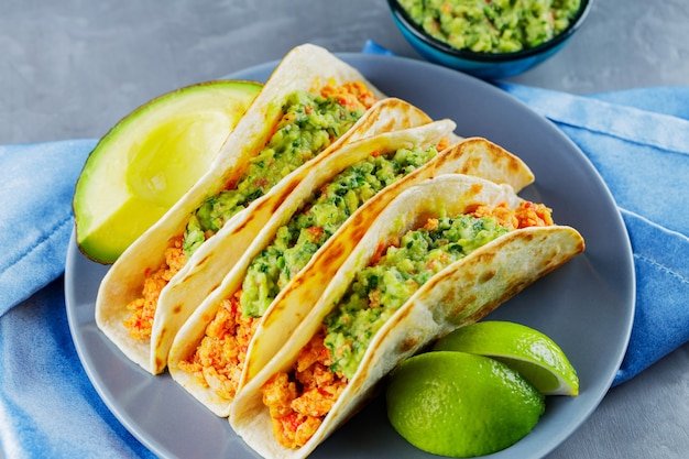 Photo tacos with fried minced meat and guacamole on a gray plate. mexican tacos and lime slices on a gray background. mexican food. copy space