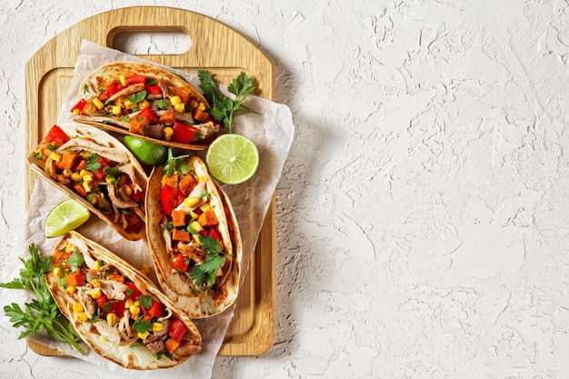 Tacos with grilled chicken meat corn roasted sweet potatoes cubes red pepper  and parsley served  on a wooden board on  a white concrete table flat lay free space