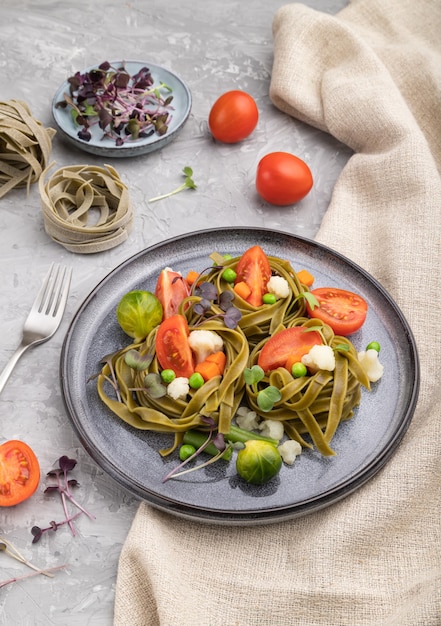 Tagliatelle green spinach pasta with tomato, pea and microgreen sprouts on a gray concrete surface and linen textile