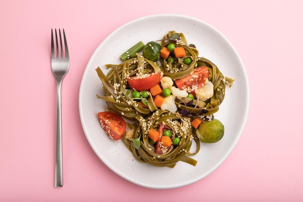 Tagliatelle green spinach pasta with tomato pea and microgreen sprouts on a pastel pink background Top view close up