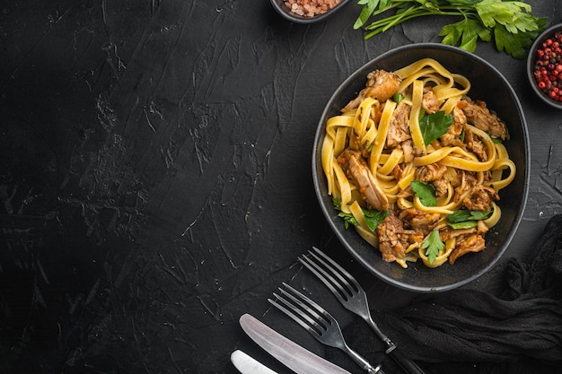 Tagliatelle with chanterelles and stewed rabbit set, in bowl, on black stone background, top view flat lay, with copy space for text