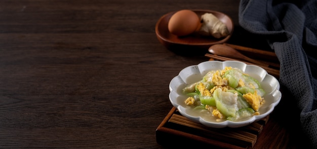 Taiwanese homemade local food of scrambled eggs with loofah gourd and sesame oil in a plate on rustic table background.