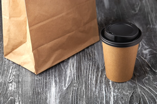 Take away paper coffee cup and lunch bag on grey wooden background