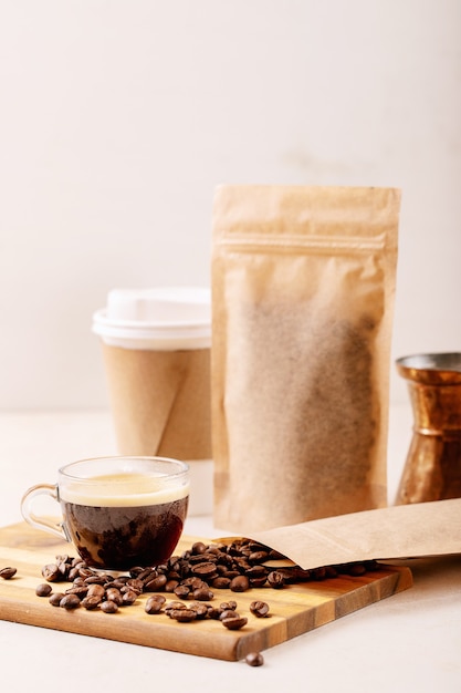 Take away paper cup, coffee beans, cup of glass espresso, copper cezve and coffee packs with blank space for logo over white wall. Copy space