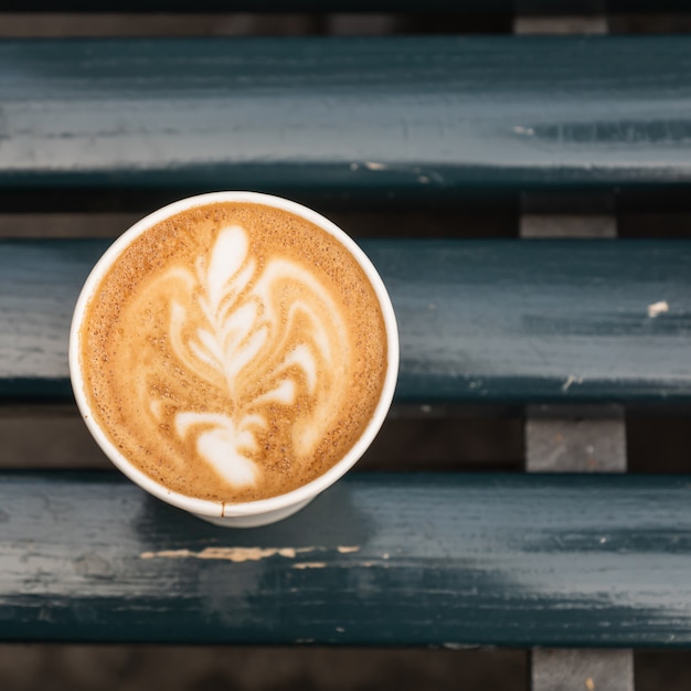 Take-away paper cup with cappuccino coffee on wooden table