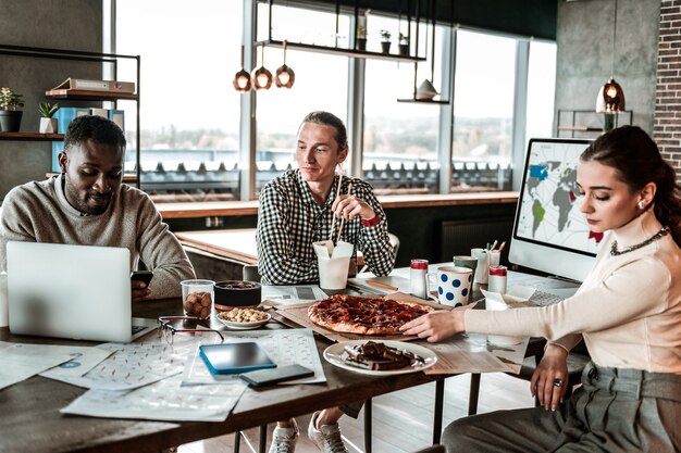 Take it. Serious blonde man sitting near his international colleague while eating Asian food