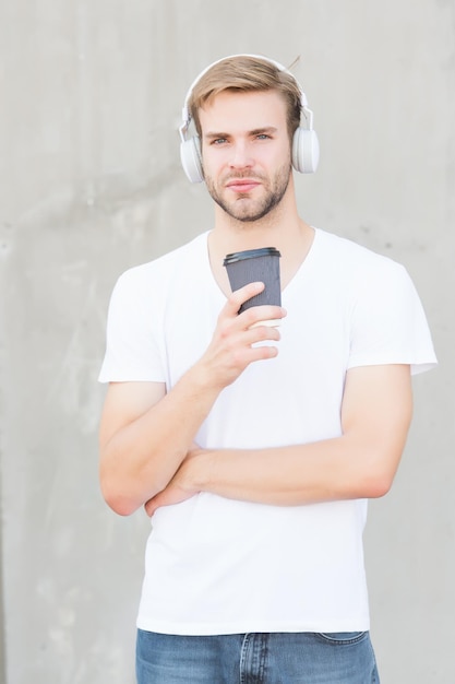 Takeaway beverage on the move Handsome man listen to music drinking coffee Young guy hold drinking cup outdoors Healthy drinking habit Drinking hot chocolate or tea Music and diet Modern life