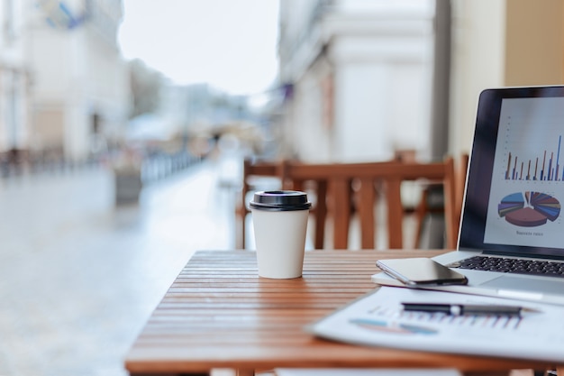 Takeaway coffee and a laptop with a financial chart on the table in the cafe .