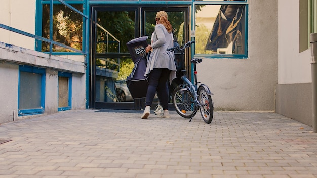 Takeaway restaurant worker giving food order package to male client at front door. African american courier delivering restaurant takeaway meal to man at building entrance, taking paperbag.