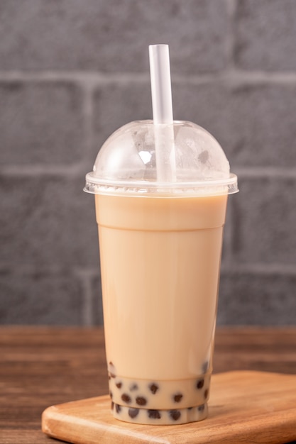 Takeout with disposable item concept popular Taiwan drink bubble milk tea with plastic cup and straw on wooden table