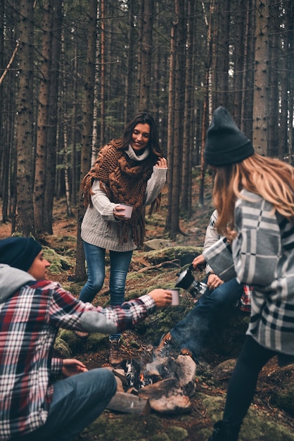 Taking care of each other. Group of happy young people standing around the campfire while hiking in the woods