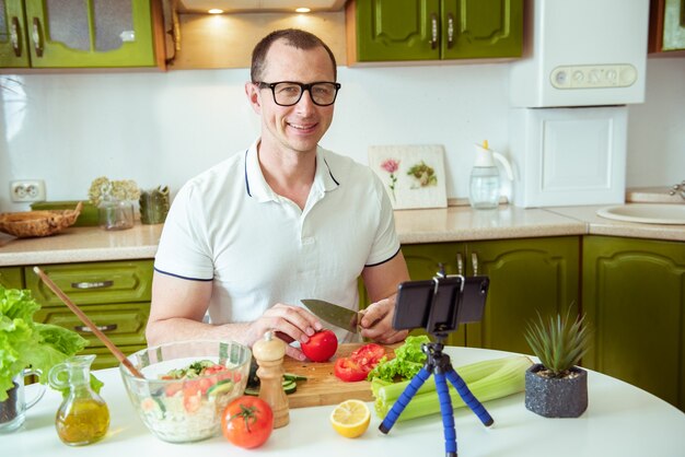 Taking care of his health. Handsome young man in casual wear looking at camera and smiling while sitting in the kitchen at home