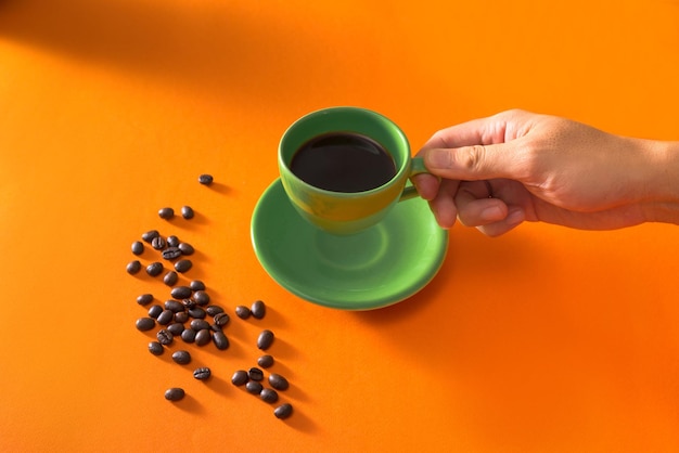 Taking green cup of coffee with coffee beans on orange background