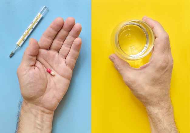 Taking medicine man hands holding a pill and a glass of water, top view