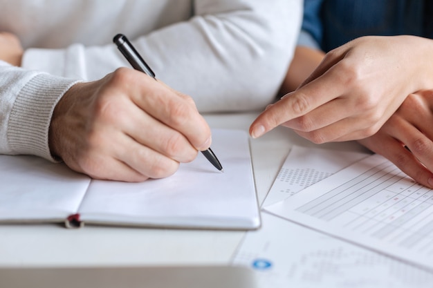 Taking notes. Close up of a pen being in hands of a nice handsome man while writing something in the notebook