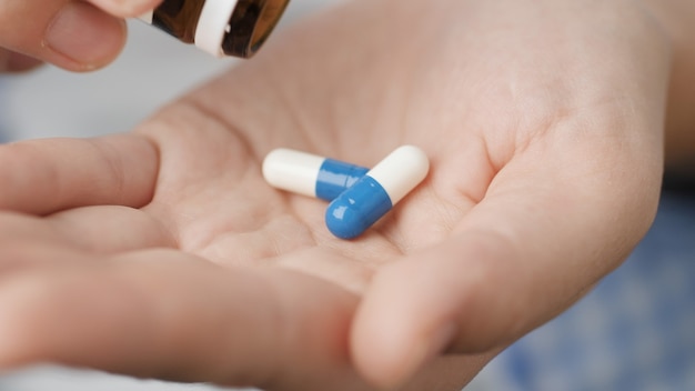 Taking pills. Two big white-blue cylindrical capsule pills fall into palm of hand from pill bottle. Close-up, front view, center composition