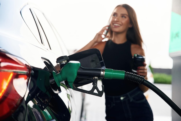 Talking by a phone A young woman at a gas station with her car