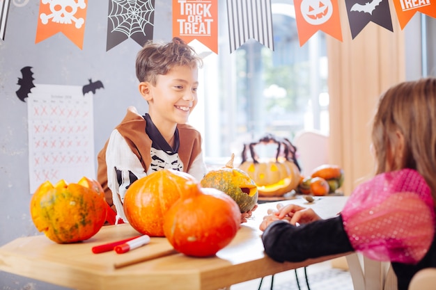 Talking to friend. Beaming funny boy wearing Halloween skeleton costume talking to his beautiful friend