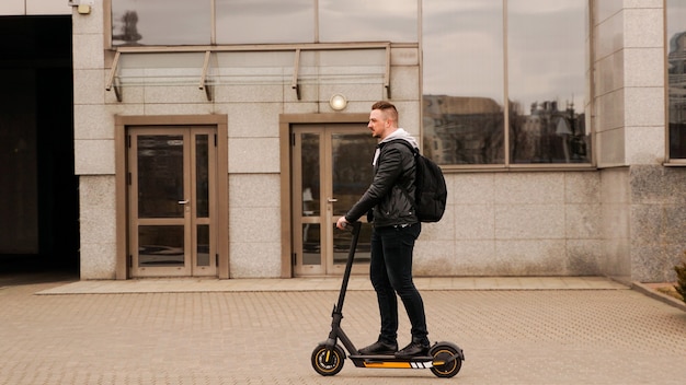 Tall man on an electric scooter against the backdrop of gray city buildings