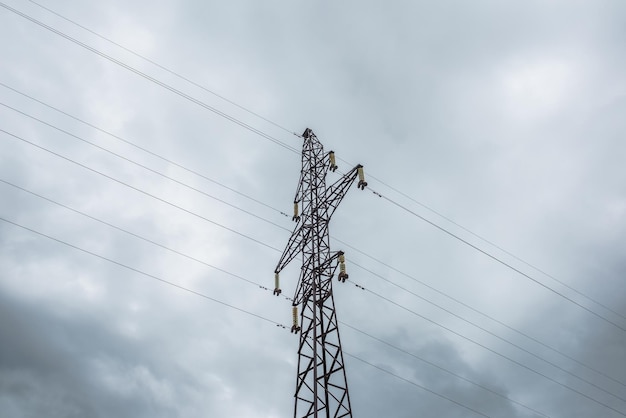 Tall tower of power lines on background of gray cloudy sky High electric tower with wires against cloudy gray sky Tower of electricity in overcast Sloudscape with power lines against gray clouds