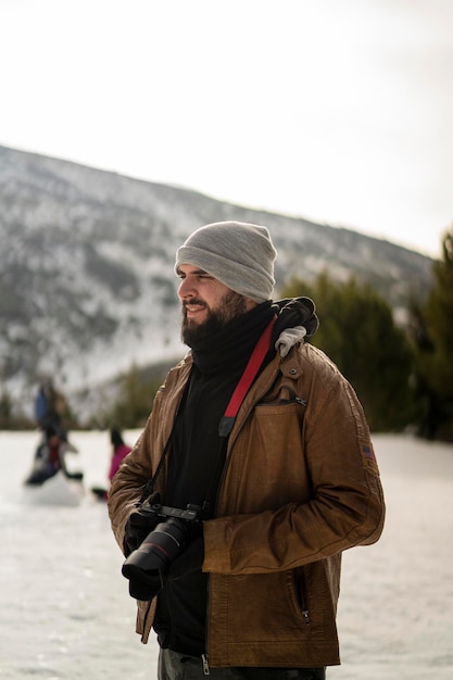 tall young guy with beard and photo camera taking pictures in the snow