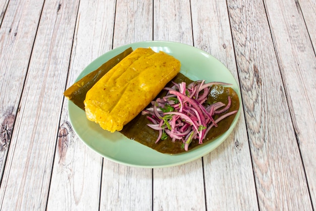 Photo tamale stuffed with pork red onion and chopped parsley on banana leaf and round green plate on wooden table