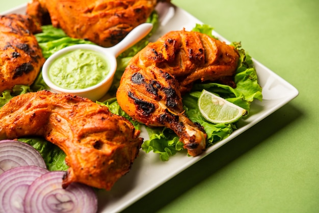 Tandoori chicken is a chicken dish prepared by roasting chicken marinated in yogurt and spices in a tandoor or a clay oven, served with onion and green chutney