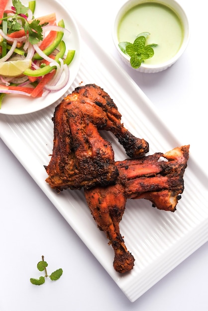 Tandoori chicken - prepared by roasting chicken marinated in yoghurt and spices in a tandoor. Leg pieces served in a plate with salad & chutney