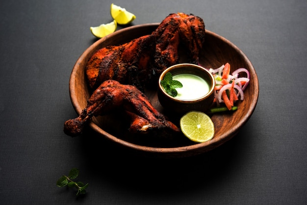 Tandoori chicken - prepared by roasting chicken marinated in yoghurt and spices in a tandoor. Leg pieces served in a plate with salad & chutney